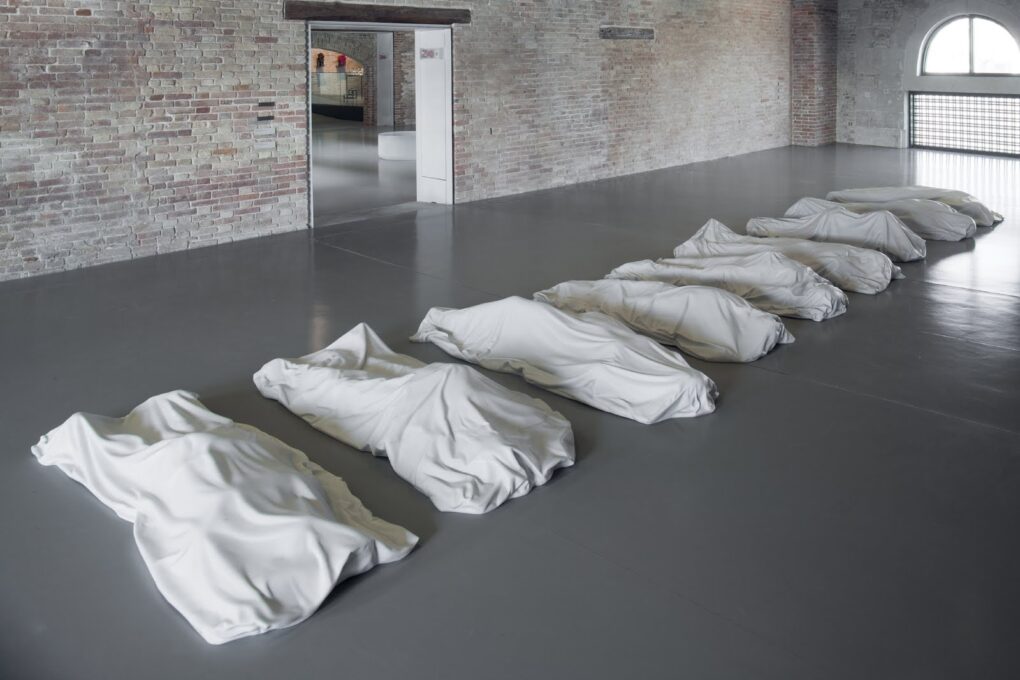 白いカッラーラ大理石でできた匿名の死者を象徴する9体の死体袋を示唆する『All』。死は誰にでも訪れるものであるという現実を示唆する。クレジット：Communication Design