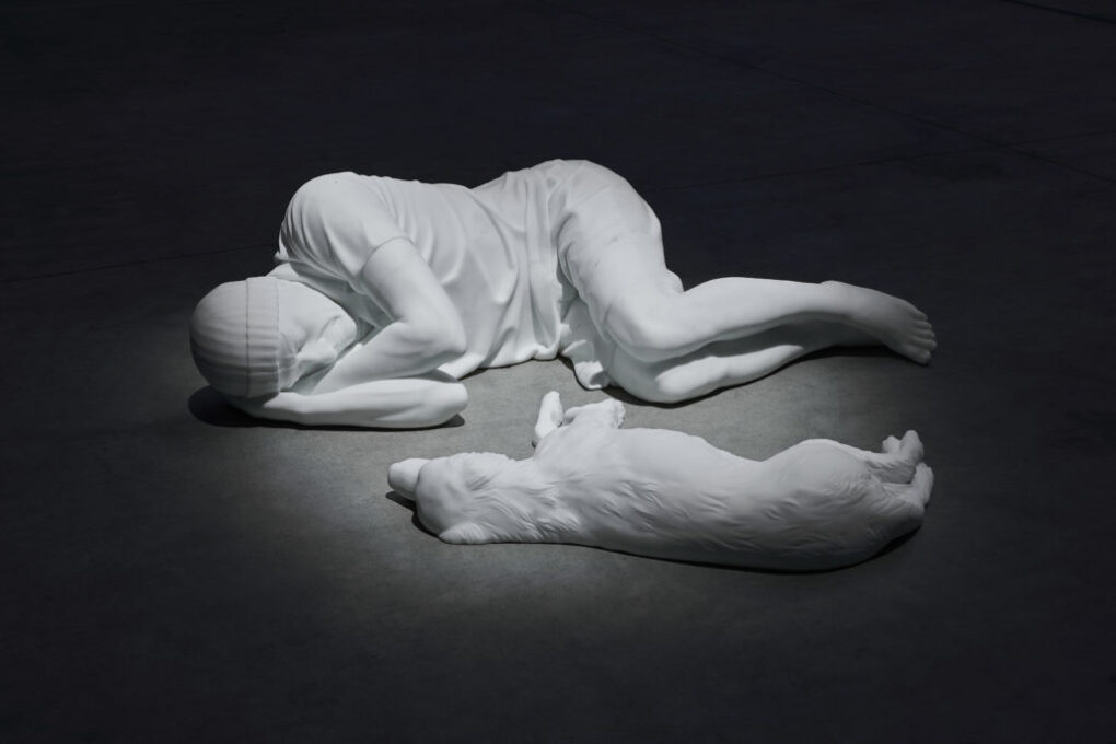 『Breath』(2021) マウリツィオ・カテラン『Breath Ghosts Blind （和訳：呼吸、幽霊、盲目）』展より（HANGAR BICOCCA） 暗闇に静かに横たわる男性と犬の等身大彫刻が、生と死、孤独と共生を静かに問いかける。

