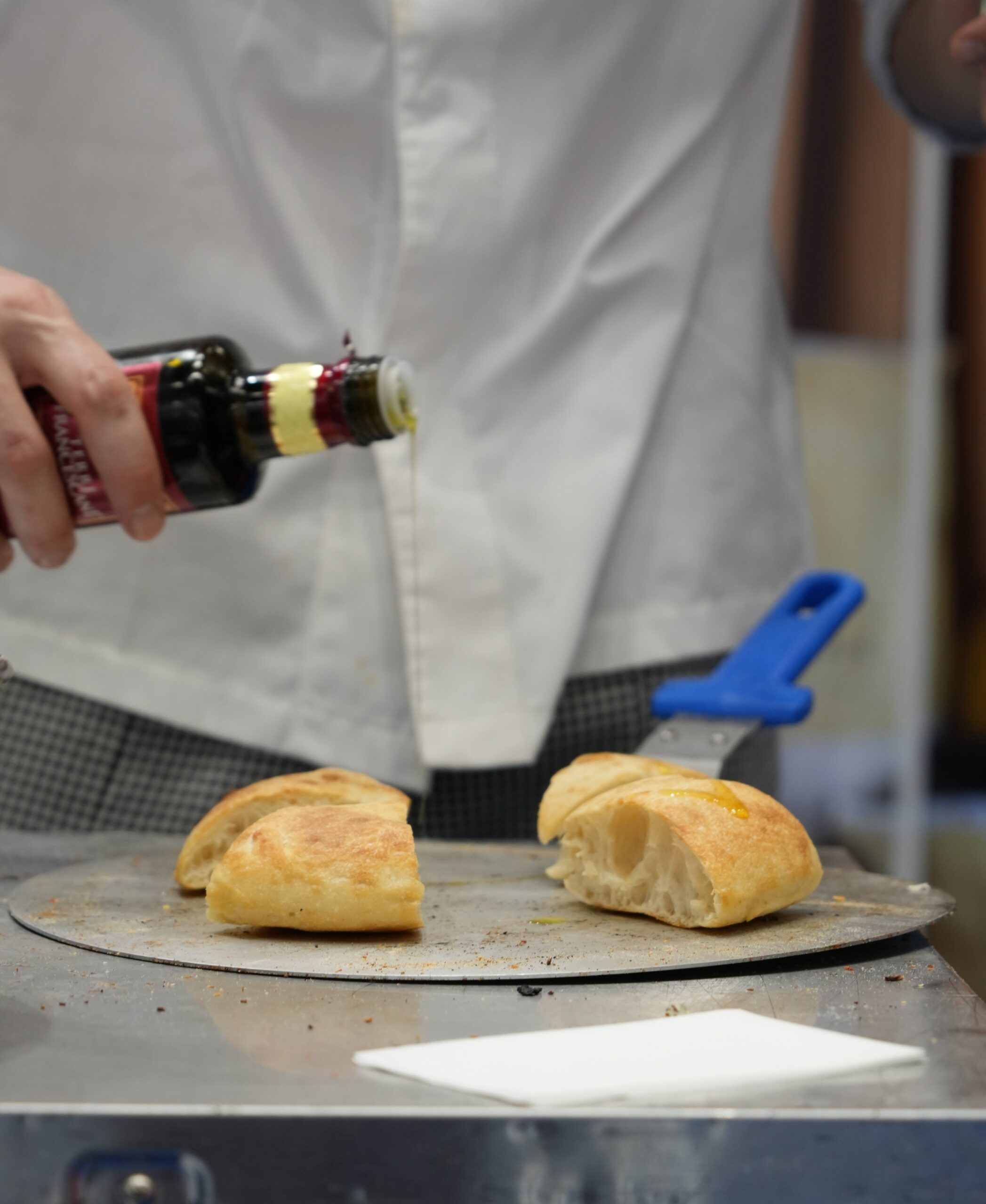 焼いたフォカッチャにオリーブオイルをかける様子